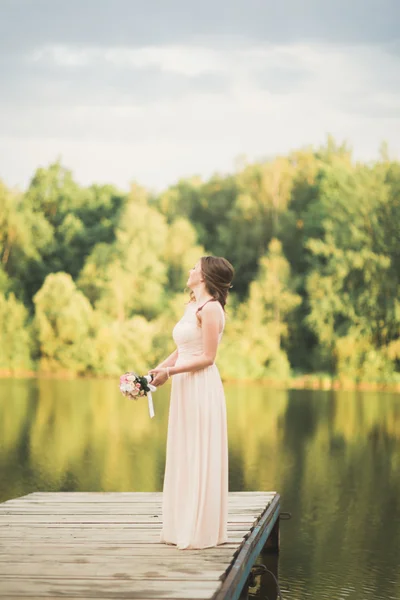 Linda noiva em vestido elegante segurando buquê posando perto da floresta e do lago — Fotografia de Stock