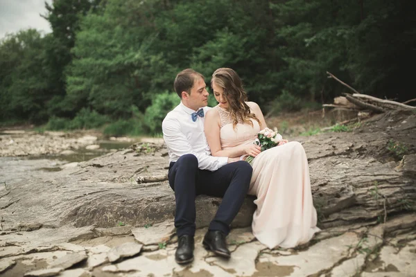 Elegante noivo elegante doce e noiva perto do rio com pedras. Casamento casal apaixonado — Fotografia de Stock