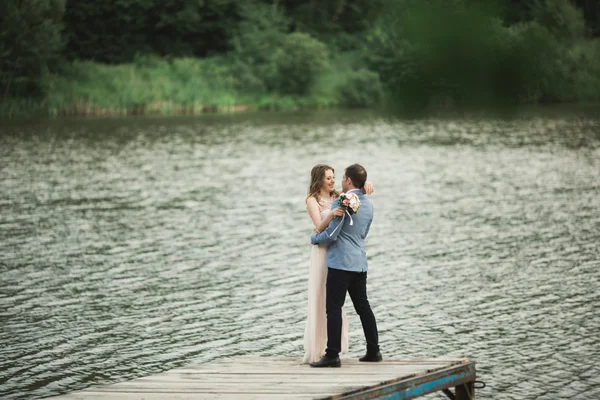 Eleganta vackra bröllop par poserar nära en sjö vid solnedgången — Stockfoto