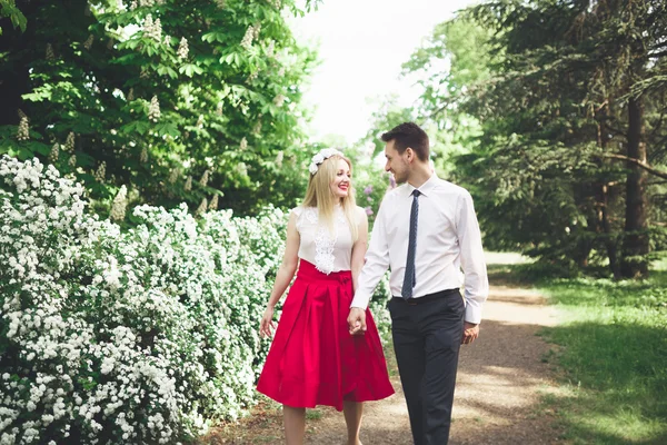 Joven hermosa pareja besándose y abrazándose cerca de los árboles con flor en el parque de verano —  Fotos de Stock