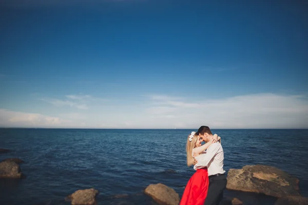 Ρομαντικό ζευγάρι ερωτευμένων που παρουσιάζουν στις πέτρες κοντά στη θάλασσα, μπλε ουρανό — Φωτογραφία Αρχείου