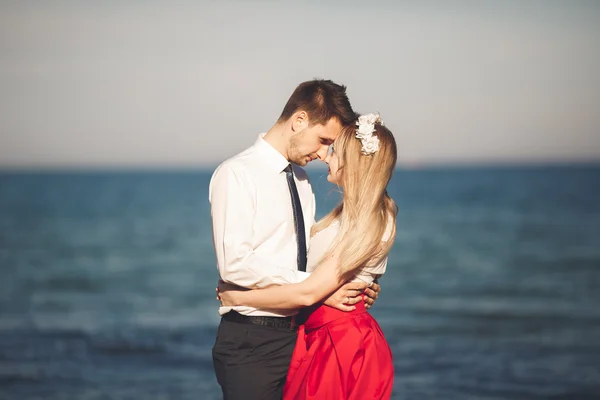 Junges glückliches Paar, das lächelnd am Strand spaziert und sich umschlingt. Liebesgeschichte — Stockfoto