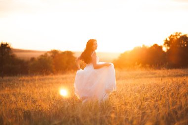 Mutlu, güzel, genç gelin gün batımında bir çayırda.
