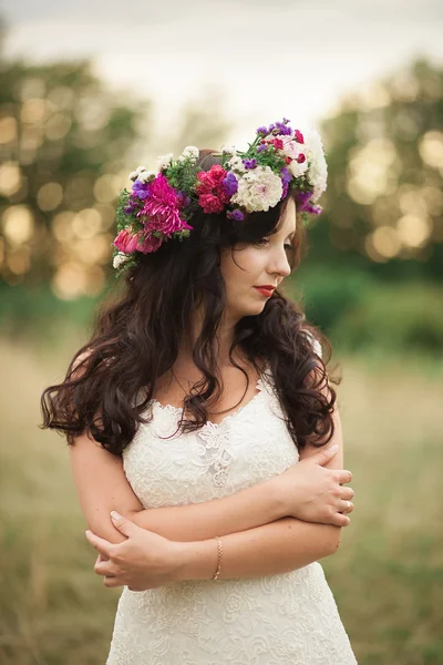 Noiva. Mulher loira jovem bonita no parque com coroa de flores e buquê em um dia quente de verão — Fotografia de Stock