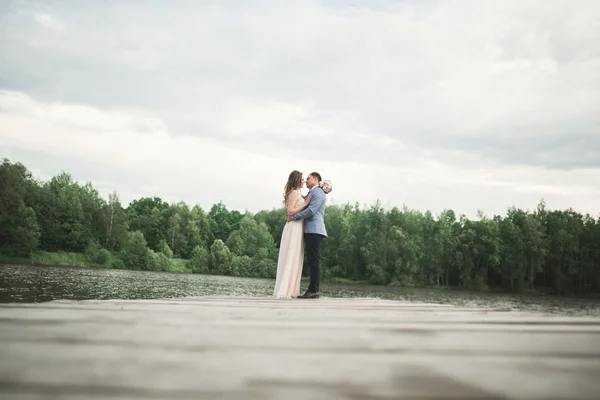 Κομψή κομψό γαμπρό με του χαρούμενος πανέμορφη μελαχρινή νύφη στο φόντο μιας λίμνης — Φωτογραφία Αρχείου