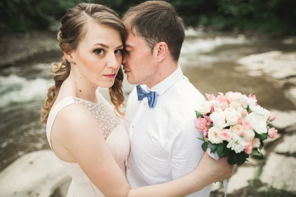 คู่แต่งงานที่มีความสุขกอดและยิ้มกันบนพื้นหลังทะเลสาบป่า — ภาพถ่ายสต็อก