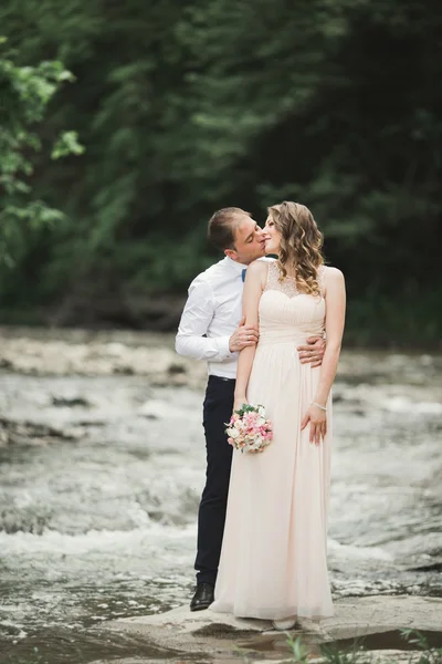 エレガントな優しいスタイリッシュな新郎と花嫁の石と川の近く。愛の結婚式のカップル — ストック写真