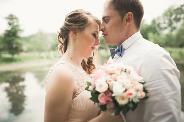 Novia y novio celebrando hermoso ramo de bodas. Lago, bosque — Foto de Stock