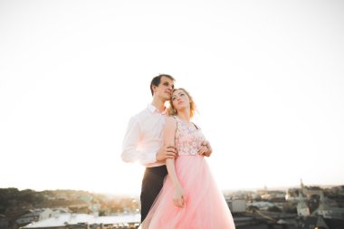 Çatıda mükemmel şehir manzaralı elele ve sarılma poz aşık genç bir çift. Güzel gün batımı