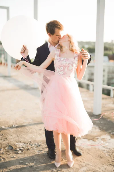 Pareja joven enamorada posando en el techo con una vista perfecta de la ciudad cogida de la mano y abrazándose. Hermoso atardecer —  Fotos de Stock