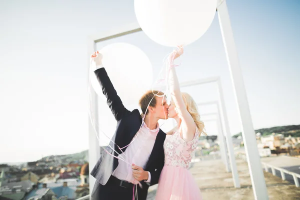 Retrato al aire libre bastante soleado de pareja joven y elegante mientras se besa en el techo con vista a la ciudad —  Fotos de Stock