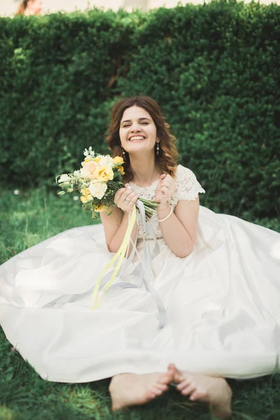 Bella sposa seduta a terra con un bouquet sorridente alla macchina fotografica — Foto Stock