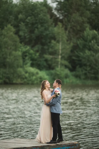 Elegante elegante novio con su hermosa novia morena feliz en el fondo de un lago — Foto de Stock