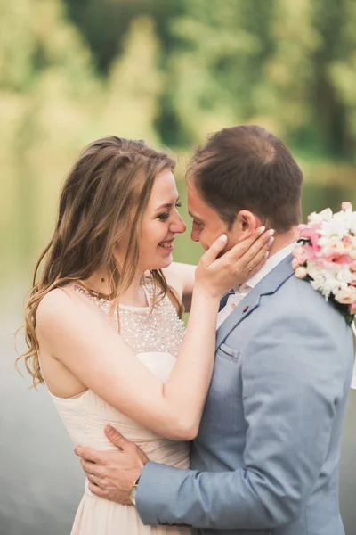 Elegante hermosa pareja de boda posando cerca de un lago al atardecer —  Fotos de Stock