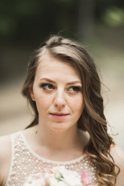 Magnifique mariée en robe élégante tenant bouquet posant près de la forêt et du lac — Photo