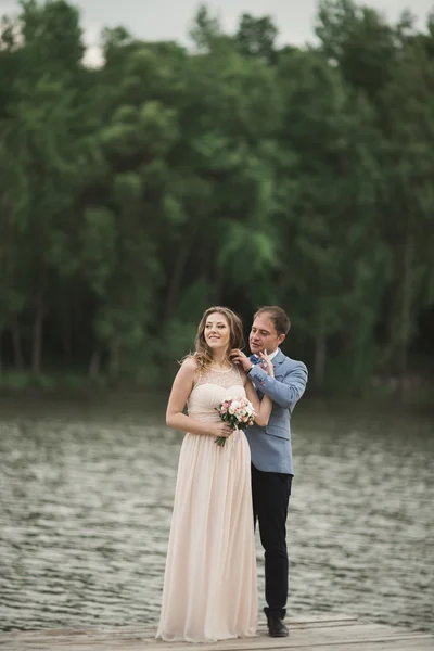 Elegante hermosa pareja de boda posando cerca de un lago al atardecer —  Fotos de Stock