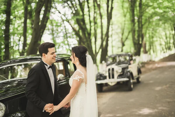 Счастливая молодожёны, муж и жена целуются возле стильного ретро-автомобиля — стоковое фото