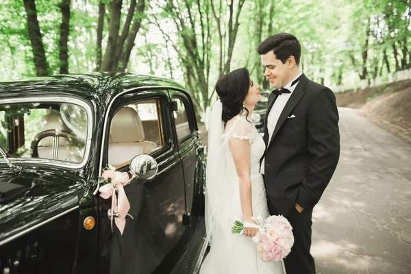 Hermosa pareja recién casada posando cerca de coche negro retro — Foto de Stock