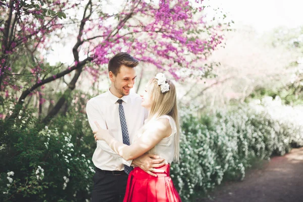 Genç güzel çift öpüşme ve ağaçları ile çiçeği yaz Park yakınındaki sarılma — Stok fotoğraf
