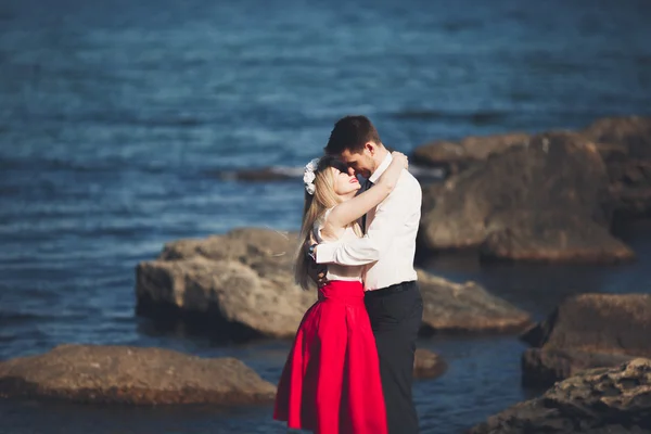 Romantische verliefde paar poseren op stenen in de buurt van de zee, blauwe hemel — Stockfoto