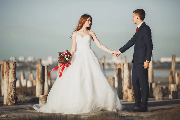 Casal de casamento, noivo, noiva com buquê posando perto do mar ao pôr do sol — Fotografia de Stock