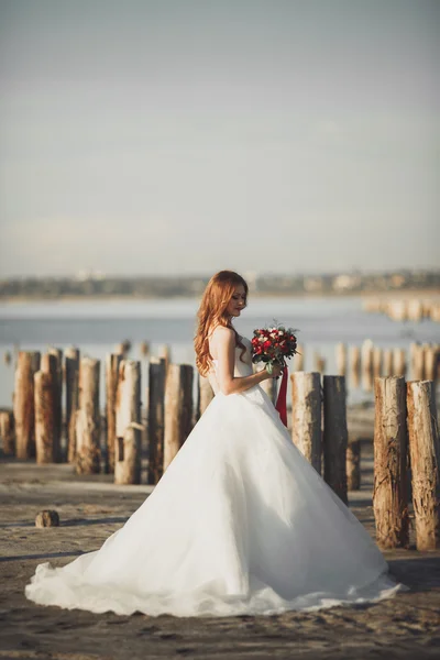 Bella dama, novia posando en un vestido de novia cerca del mar al atardecer —  Fotos de Stock