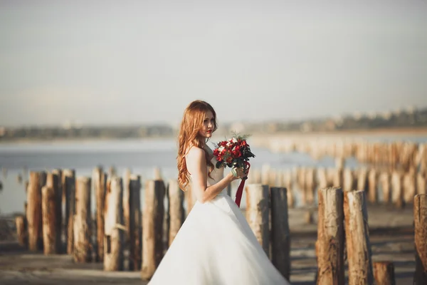 Bella signora, sposa in posa in un abito da sposa vicino al mare al tramonto — Foto Stock