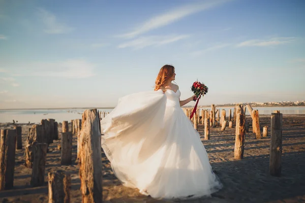 아름다운 아가씨, 해 가 지면 해변에서 웨딩 드레스를 입고 포즈를 취하는 신부 — 스톡 사진