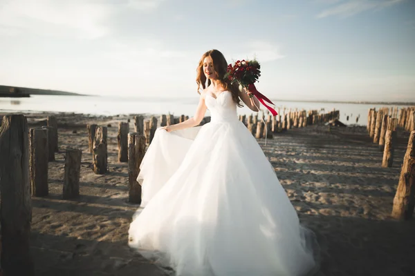 Bella giovane sposa con bouquet da sposa in posa sullo sfondo mare — Foto Stock