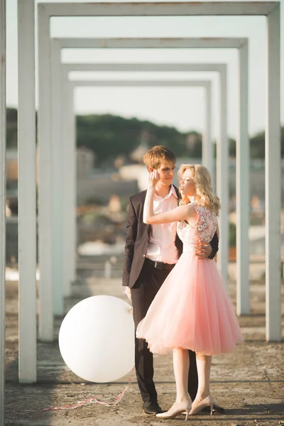 Retrato ao ar livre muito ensolarado de jovem casal elegante enquanto se beija no telhado com vista para a cidade — Fotografia de Stock