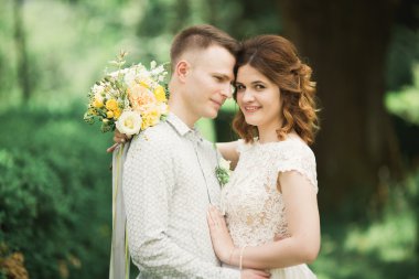 Yeni evli çiftimiz düğün günlerinde ellerinde buketle parkta yürüyorlar.