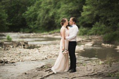 Zarif nazik şık damat ve gelin taşlarla Nehri yakınında. Evlilik çift aşık