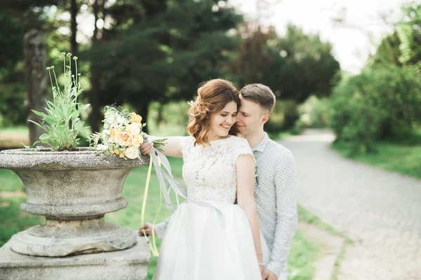 Stijlvol paar gelukkige pasgetrouwden wandelen in het park op hun trouwdag met boeket — Stockfoto