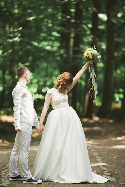 Stílusos pár boldog friss házasok sétál a parkban az esküvő napján csokorral — Stock Fotó