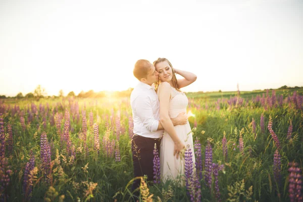Emotionele mooie bruid knuffelen kersverse bruidegom achter de zonsondergang op een veld closeup — Stockfoto