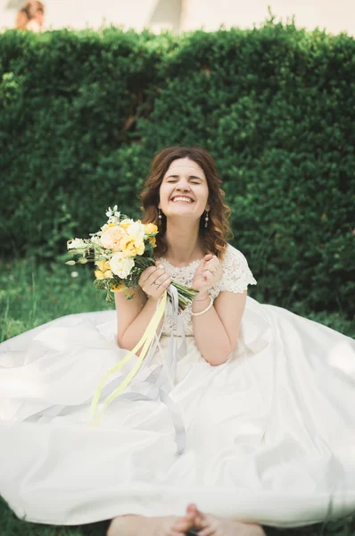 Preciosa novia sentada en el suelo sosteniendo un ramo sonriendo a la cámara — Foto de Stock