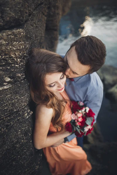 Boda pareja besándose y abrazándose en rocas cerca de mar azul — Foto de Stock