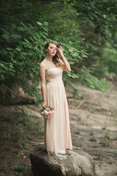 Hermosa novia joven de lujo vestido de novia de pie cerca del río con montañas en el fondo —  Fotos de Stock