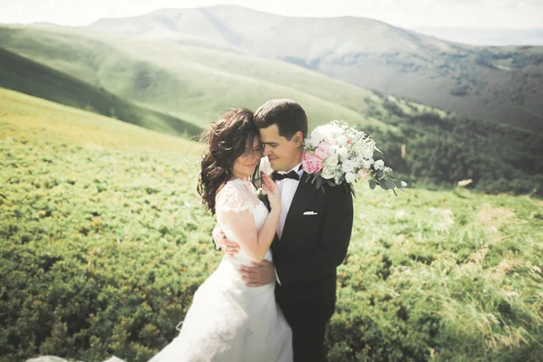 Jong pasgetrouwd stel, bruid en bruidegom zoenen, knuffelen op perfect uitzicht op de bergen, blauwe hemel — Stockfoto