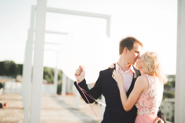 Jeune couple amoureux posant sur le toit avec vue parfaite sur la ville tenant la main et étreignant. Beau coucher de soleil — Photo