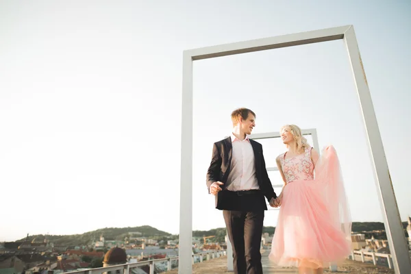 Retrato al aire libre bastante soleado de pareja joven y elegante mientras se besa en el techo con vista a la ciudad —  Fotos de Stock