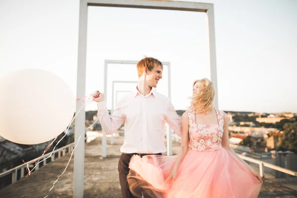 Fashion underbara vackra par poserar på tak med staden bakgrund. Ung man och sensuell blond utomhus. Livsstil. — Stockfoto