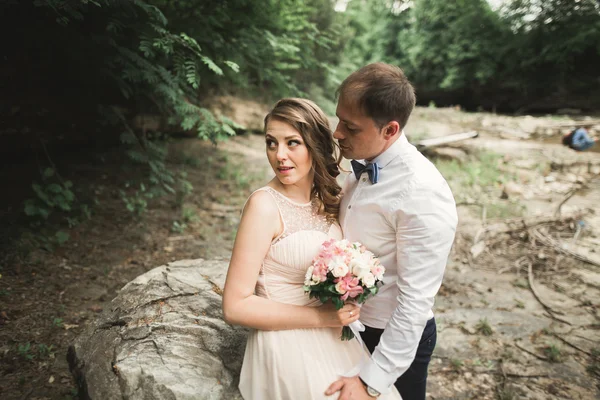 Casamento lindo casal beijando e abraçando perto da costa de um rio de montanha com pedras — Fotografia de Stock