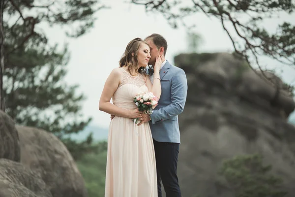 Boda pareja enamorada besándose y abrazándose cerca de rocas en hermoso paisaje — Foto de Stock