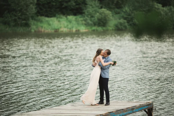 Hermosa pareja de boda, novia, novio besando y posando en el puente cerca del lago — Foto de Stock