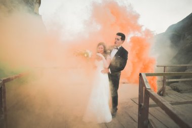 Çift yakınındaki kayaların arkasında renkli duman ile poz düğün