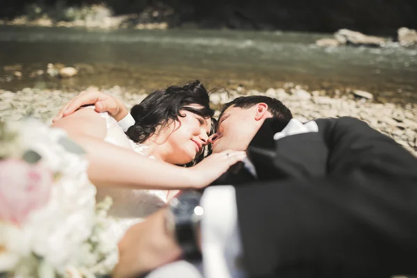 Magnifique couple de mariage embrasser et embrasser près de la rive d'une rivière de montagne avec des pierres — Photo