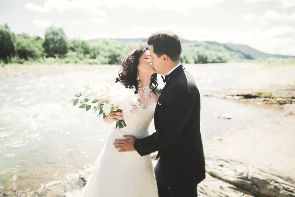 Noiva e noivo segurando lindo buquê de casamento. Posando perto do rio — Fotografia de Stock