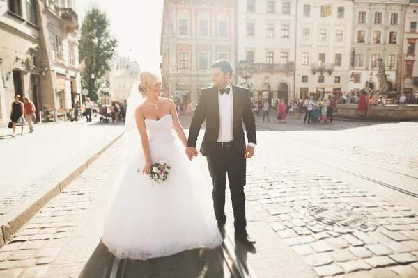Прекрасная счастливая свадебная пара, невеста с длинным белым платьем позирует в красивом городе — стоковое фото