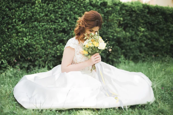 Bella sposa seduta a terra con un bouquet sorridente alla macchina fotografica — Foto Stock